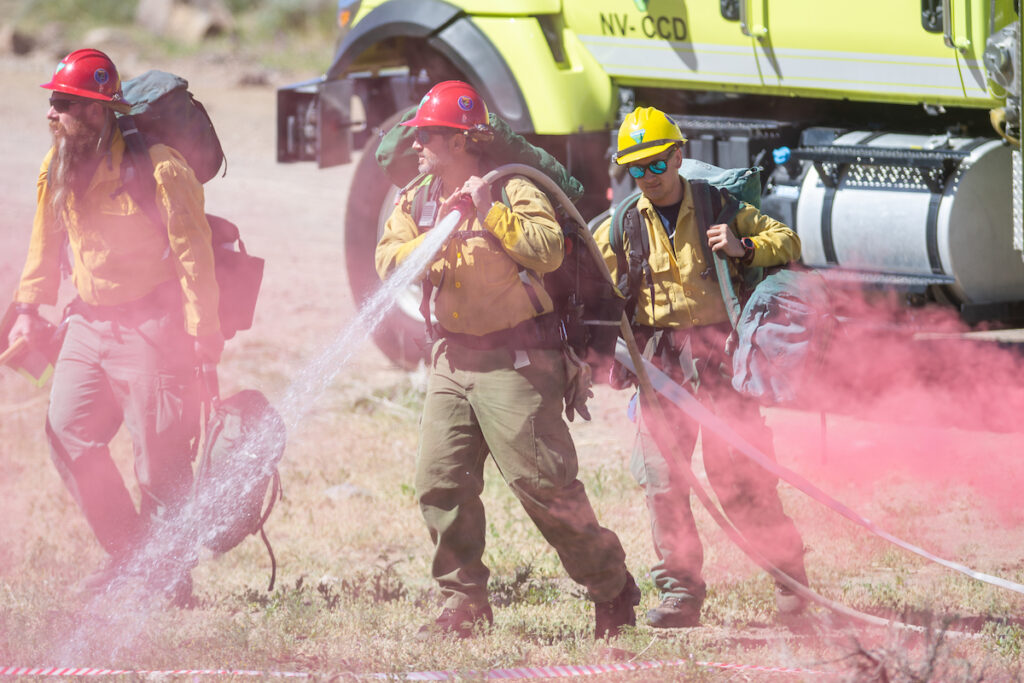 Firefighters are pictures with an active hose in the forefront and truck in the background