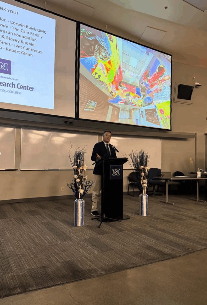 Man speaking at podium in large room with screens to his back