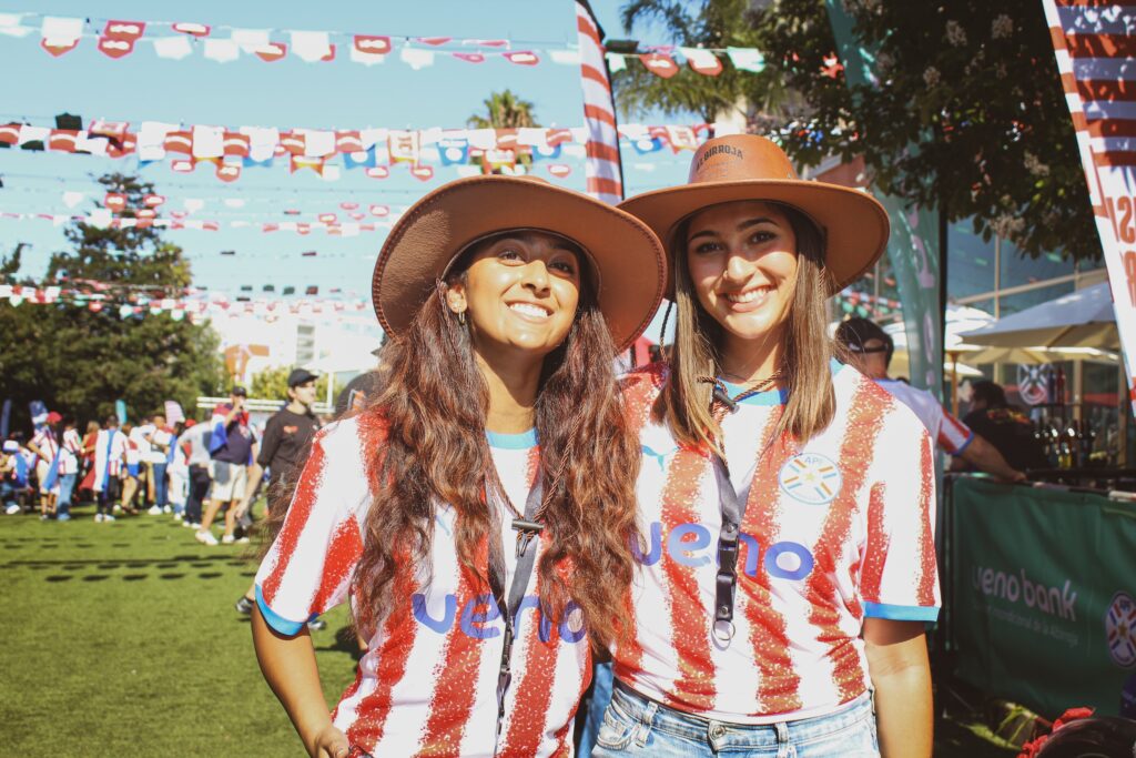 two women with hats and Paraguay soccer jersey smile at camera
