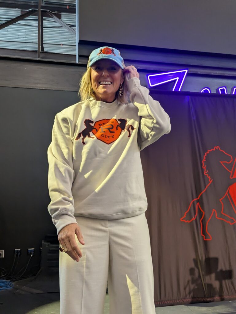 A woman is smiling and wearing clothes with the name “Reno City FC” on them