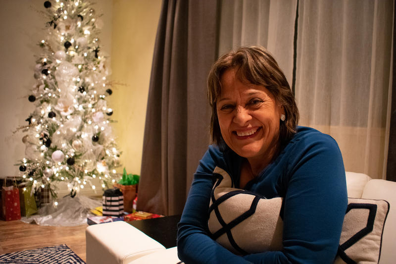 Yazmin Valenzuela, smiling while at home with their Christmas tree in the background.