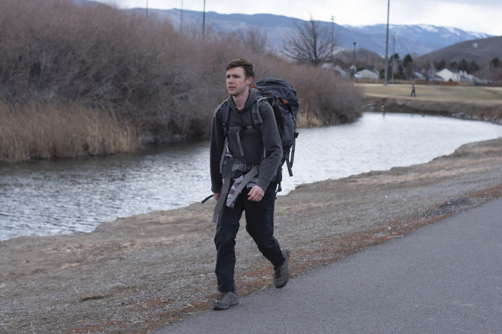 Young man with backpack walking on the side of the road.