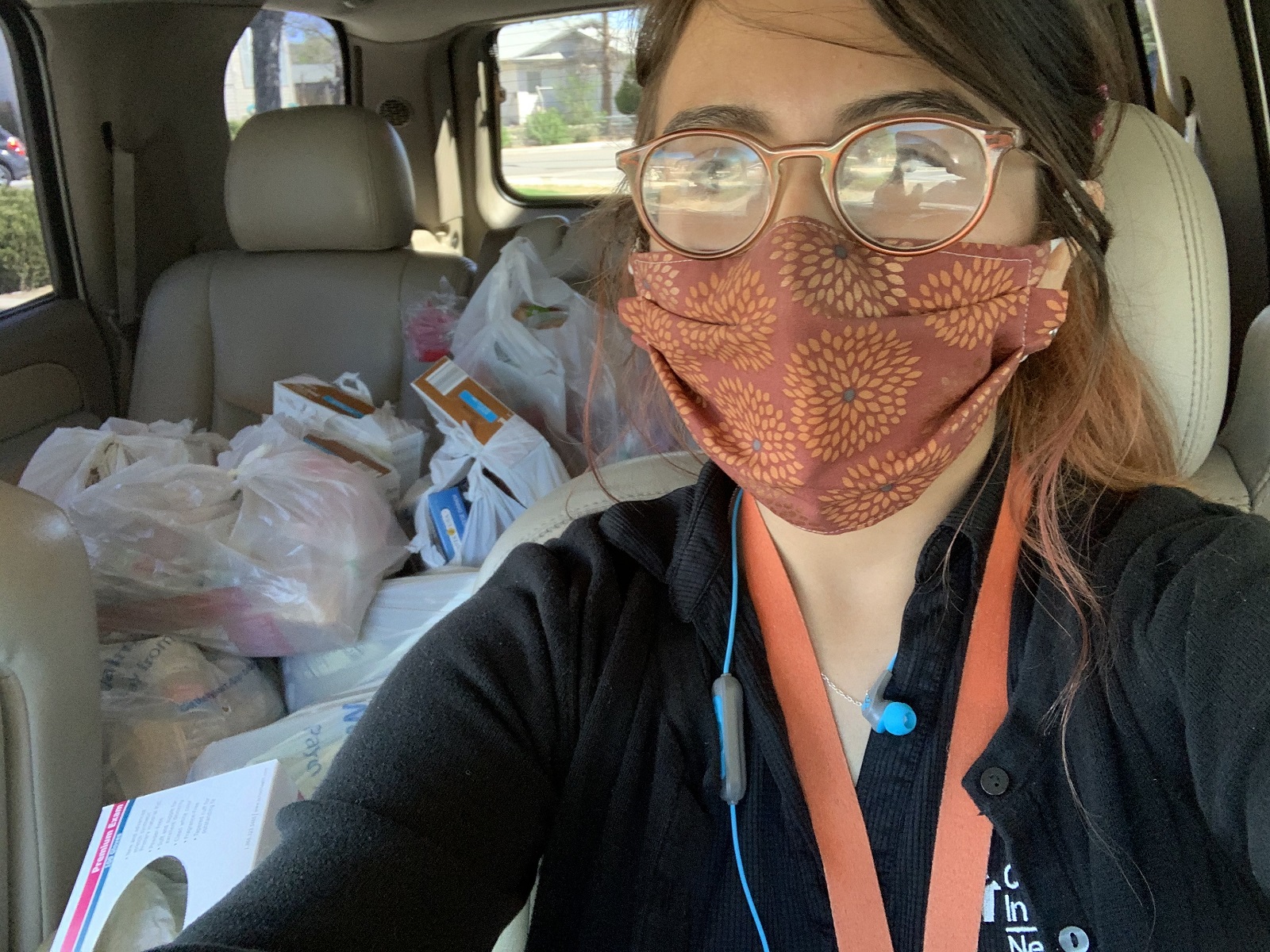 Carolina Juárez runs the Glenn Duncan Elementary food pantry. When COVID-19 it, she started delivering food to the homes of families in need. This self portrait shows a masked Carolina in her car, with bags of food piled in the back seat.