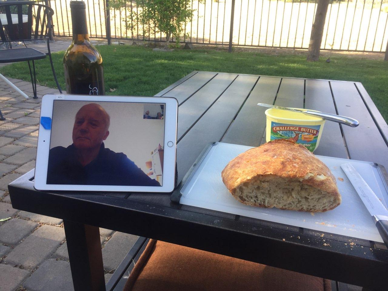 IPad on table with video image of Jim Ashurst. On table is a bottle of wine, sourdough bread and margarine.