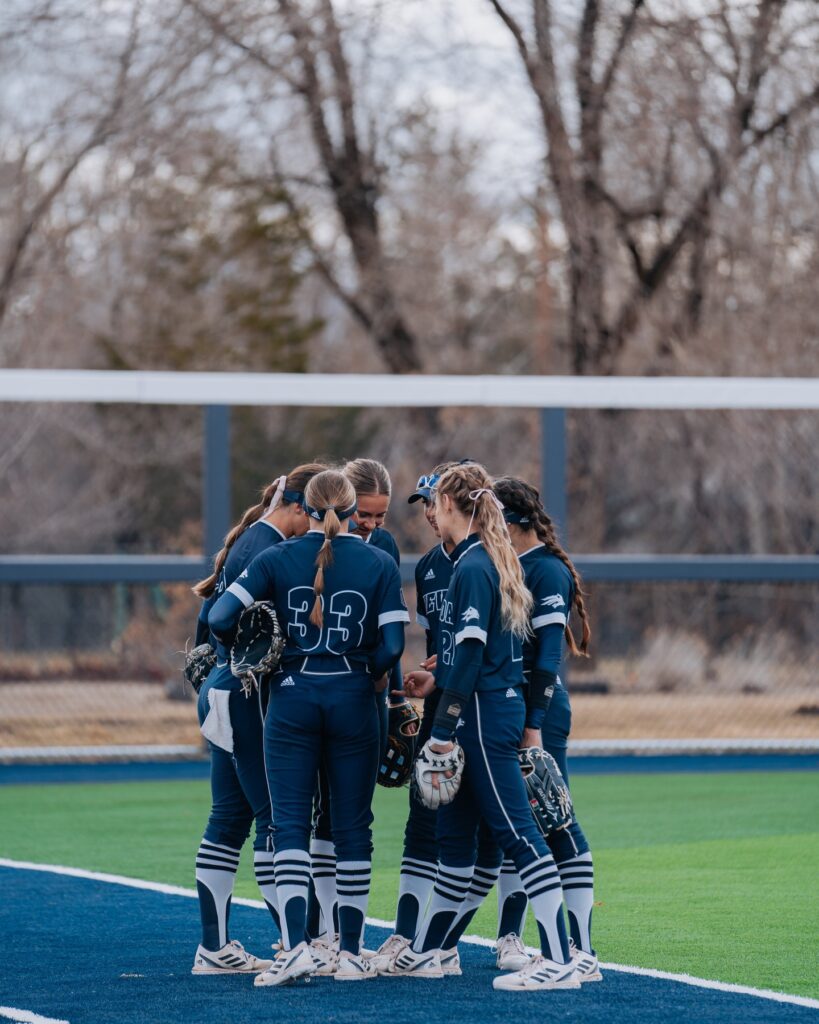 Photo of UNR softball team standing in a huddle on their field.