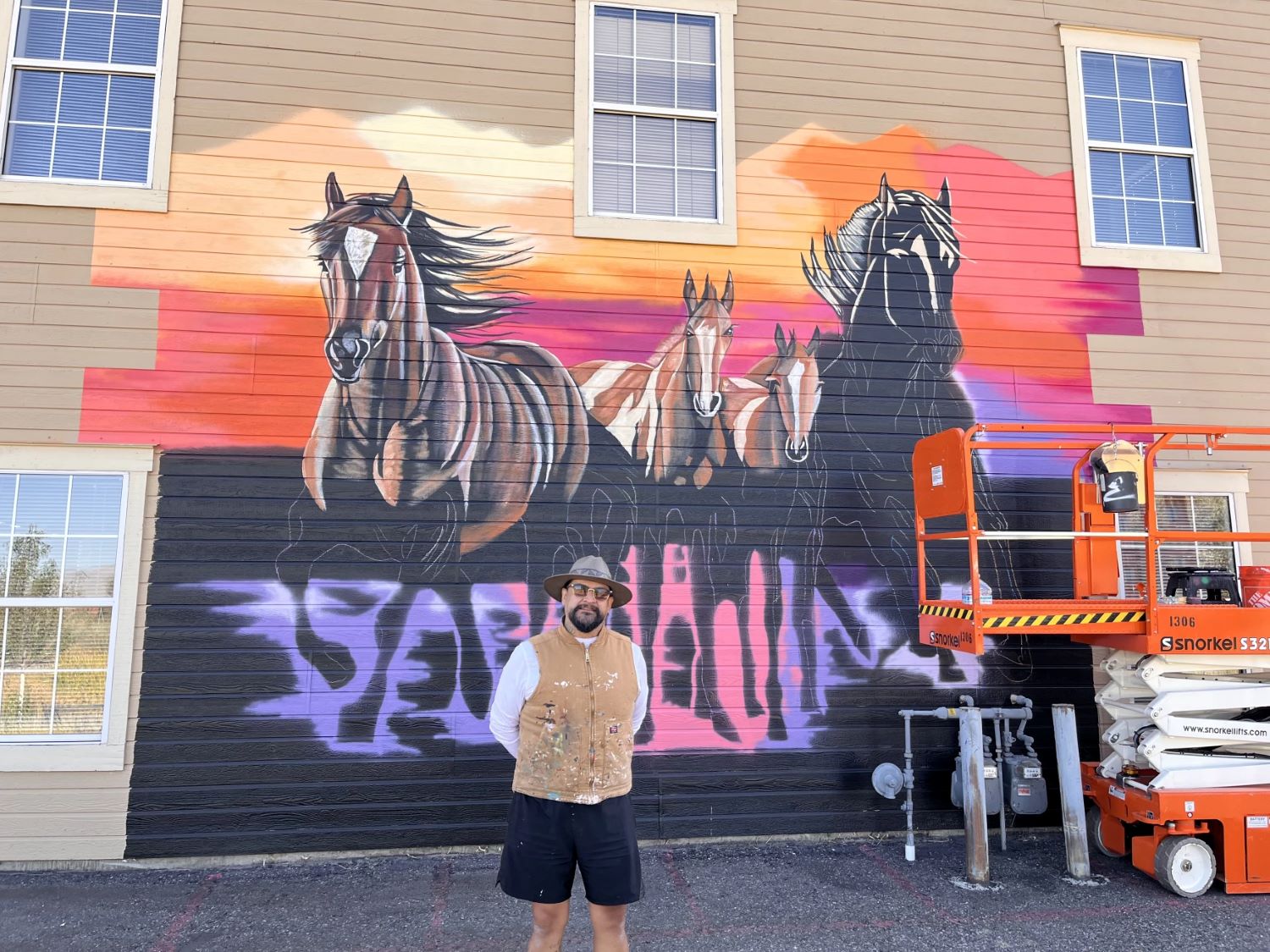 Man stands in front of mural smiling, the mural shows horses emerging in vibrant color
