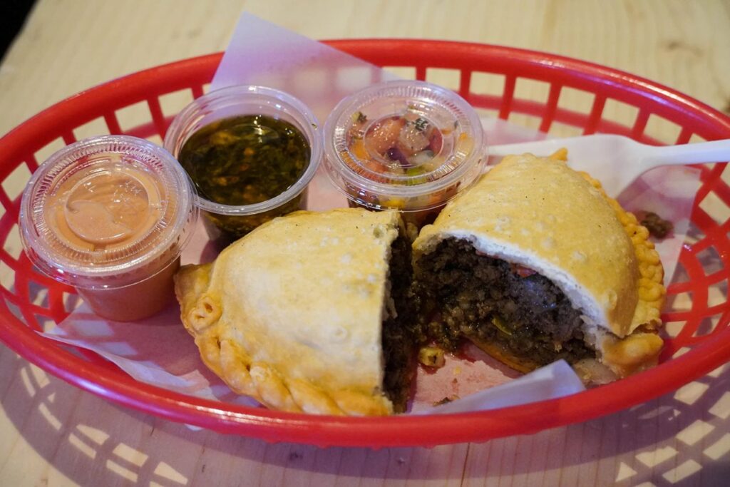 Empanada sitting in basket split open displaying the beef three different sauces