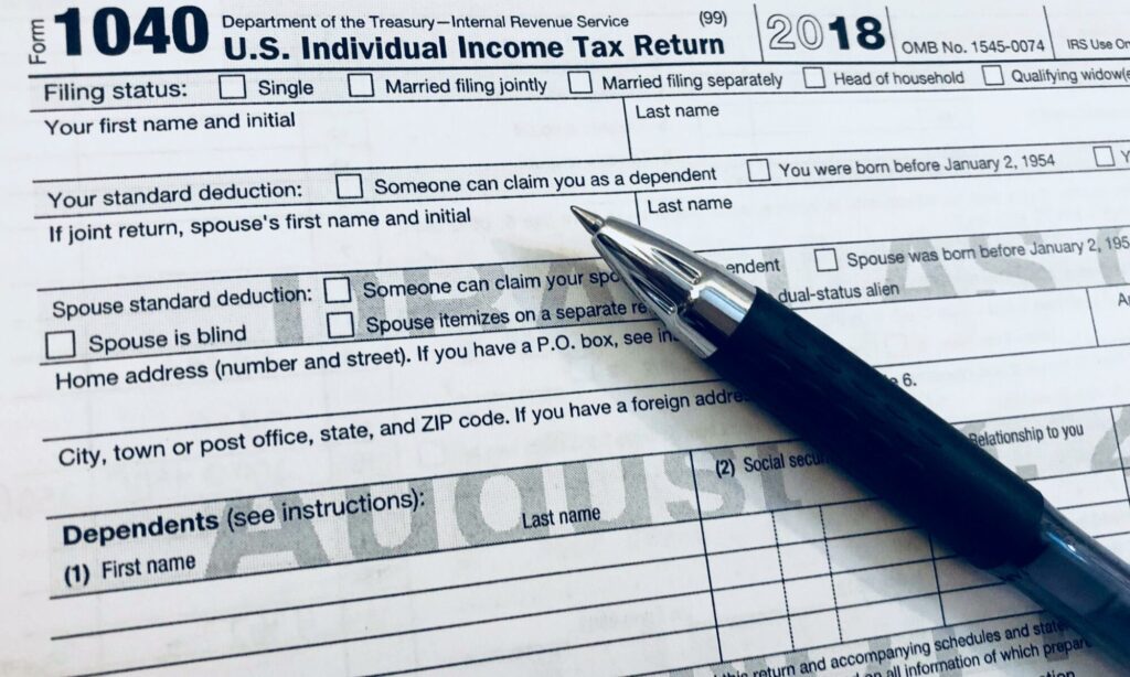 A tax form with a pen close-up is pictured.