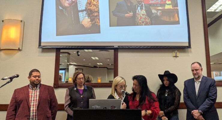six people stand at podium in front of project screen with photos