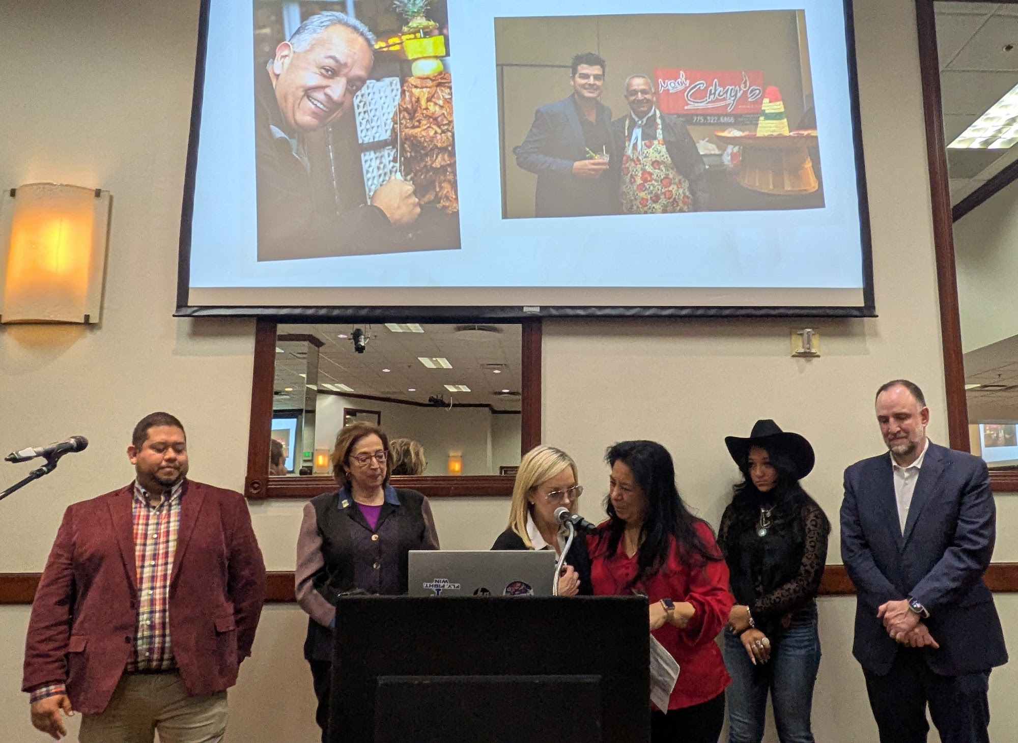six people stand at podium in front of project screen with photos