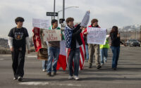 A group of students walking across a parking lot with various signs protesting ICE