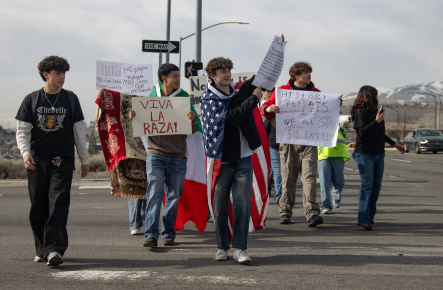A group of students walking across a parking lot with various signs protesting ICE