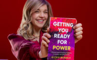 blond woman seated in red at desk holding book that says, "Getting You Ready for Power"