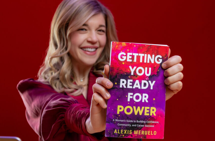 blond woman seated in red at desk holding book that says, "Getting You Ready for Power"