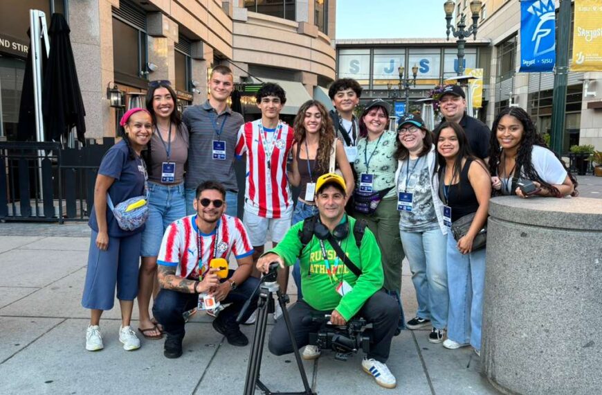 About a dozen people pose outside for a photo, some wear red and white jersey for the Paraguay soccer team.