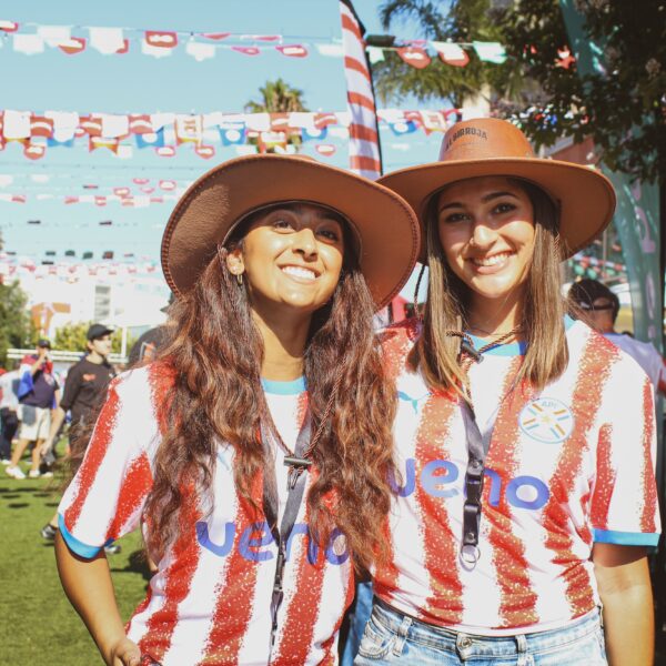 two women with hats and Paraguay soccer jersey smile at camera