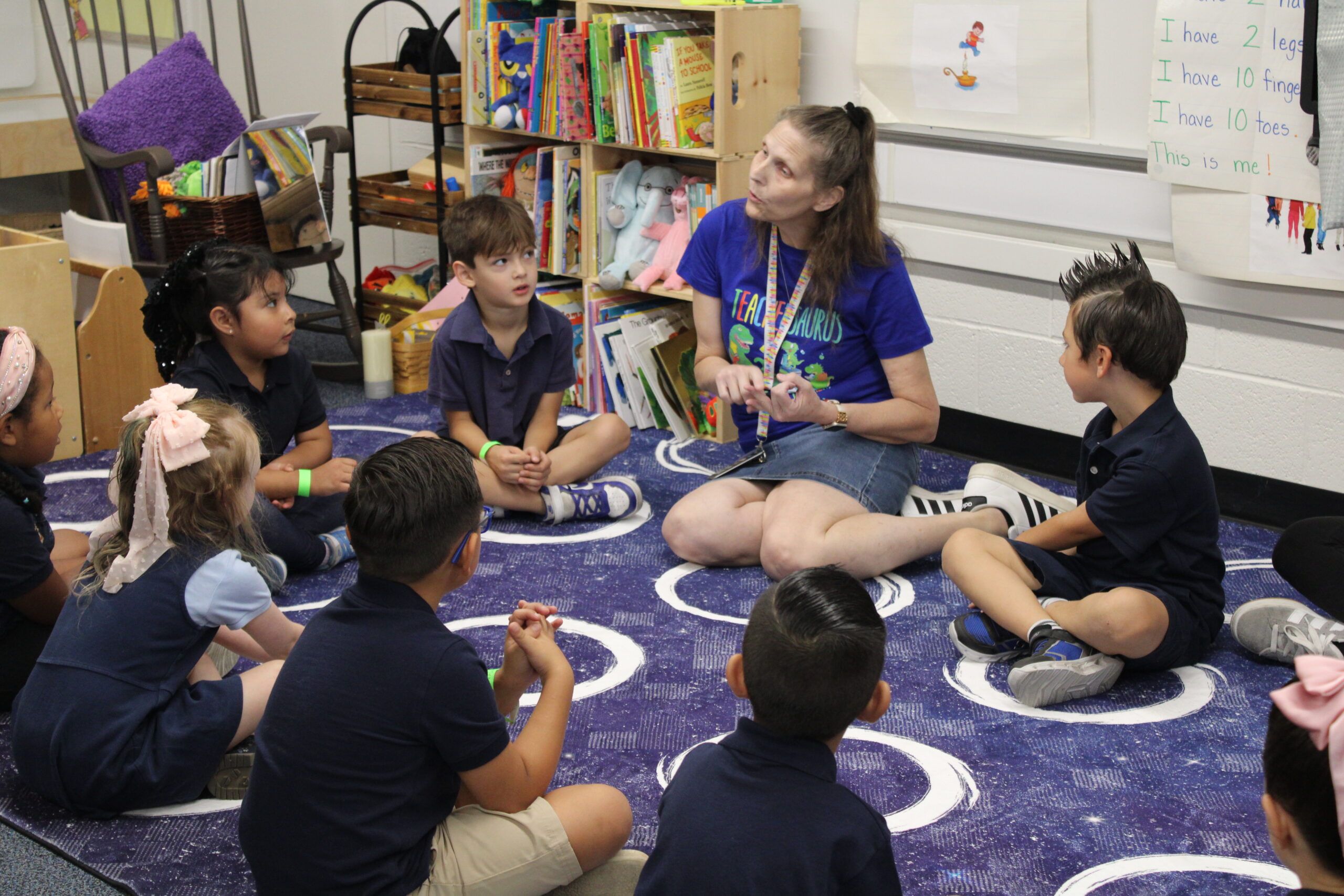 teacher sits in circle on floor with preschoolers